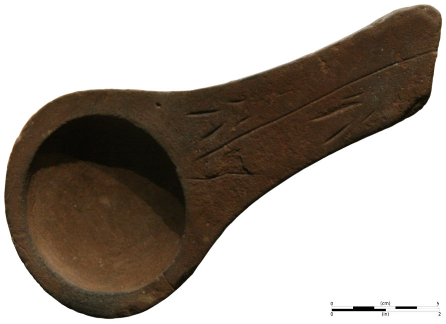 An image of a prehistoric pottery artifact, likely a bowl or scoop, made from clay. The object features a curved, shallow bowl with a handle, and it is decorated with simple linear carvings. The scale bar at the bottom indicates the size, with the artifact measuring a few centimeters in length.