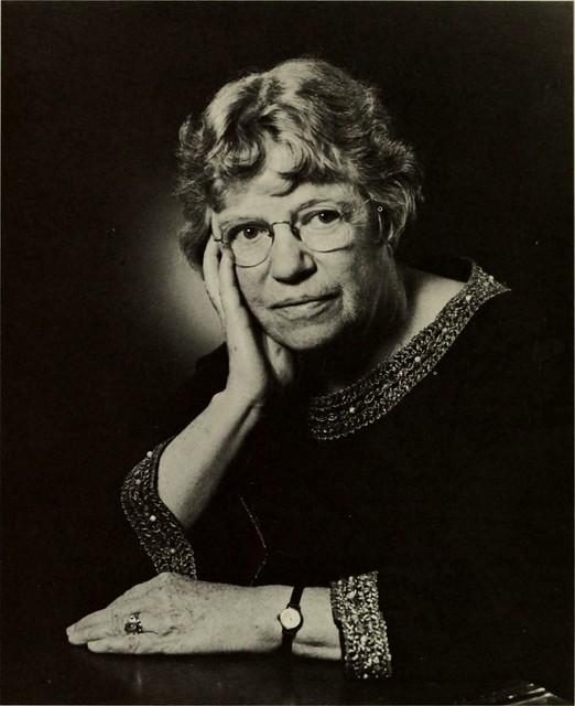 Black-and-white portrait of Margaret Mead, seated with her head resting on her hand, wearing glasses and a dark dress with decorative trim.