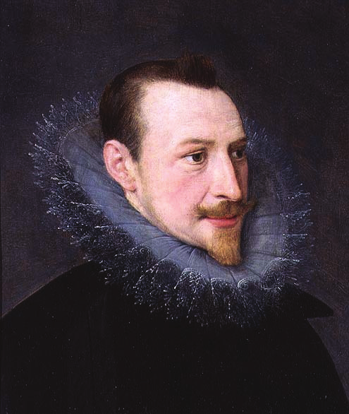 A Renaissance-era portrait of a man with short dark hair and a trimmed beard and mustache, facing slightly to the viewer’s left. He wears a dark garment with a large, elaborate ruff collar made of fine, translucent lace. The background is dark, drawing attention to the subject’s expressive face and ornate clothing.