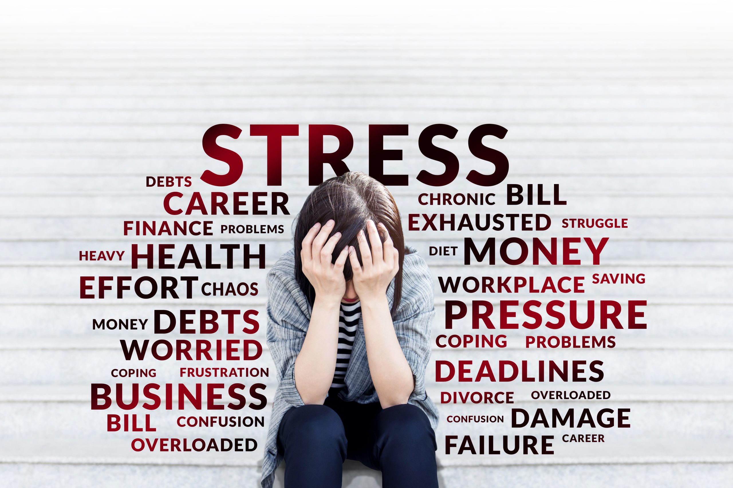 A woman sitting with her elbows on her knees and her hands on her head with the words stress words around her such as: debts, career, chronic, bill, exhausted, effort, health, business, failure, damage and deadlines. Adobe Stock