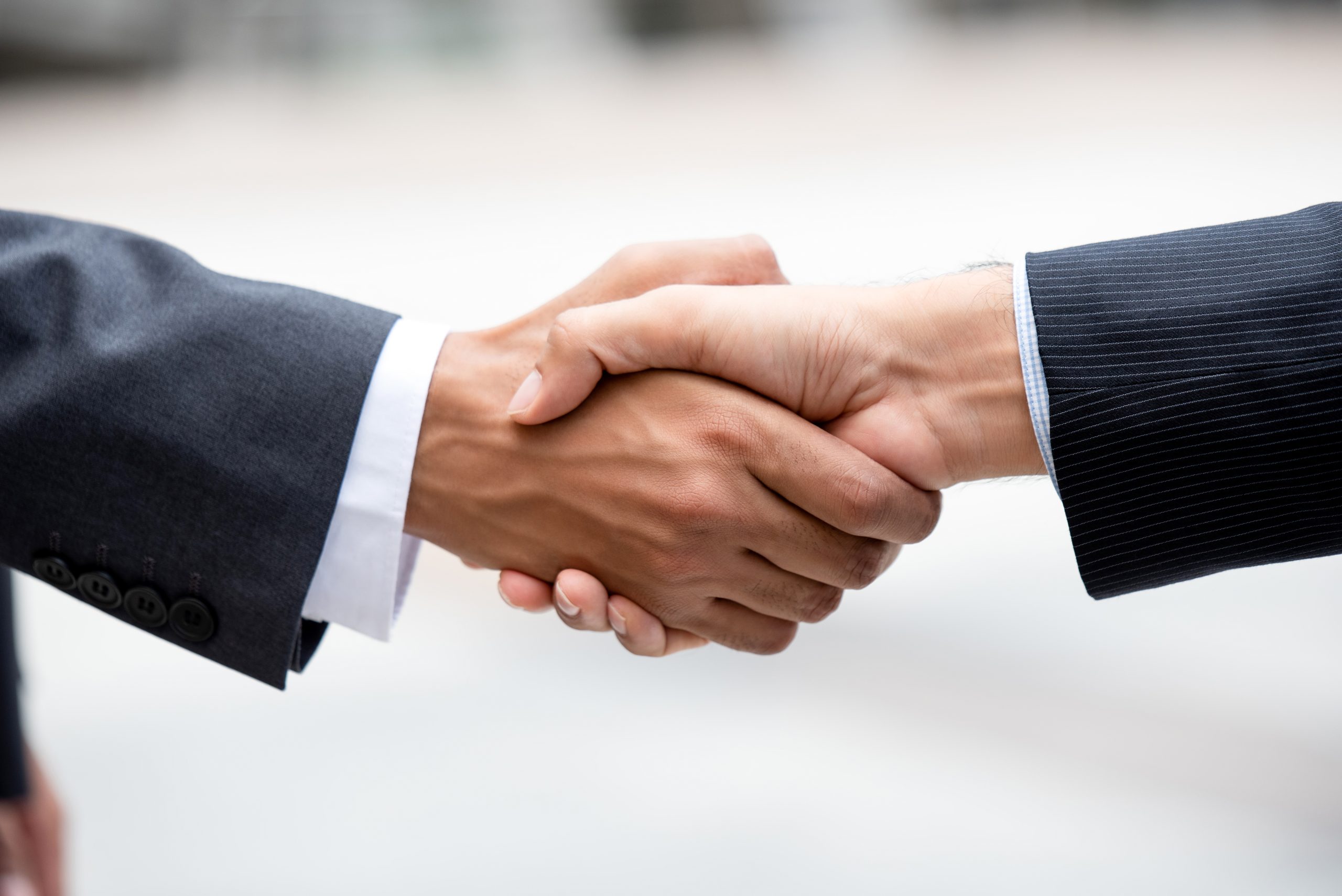 Two hands grasped in a handshake showing business jacket sleeves. Adobe Stock