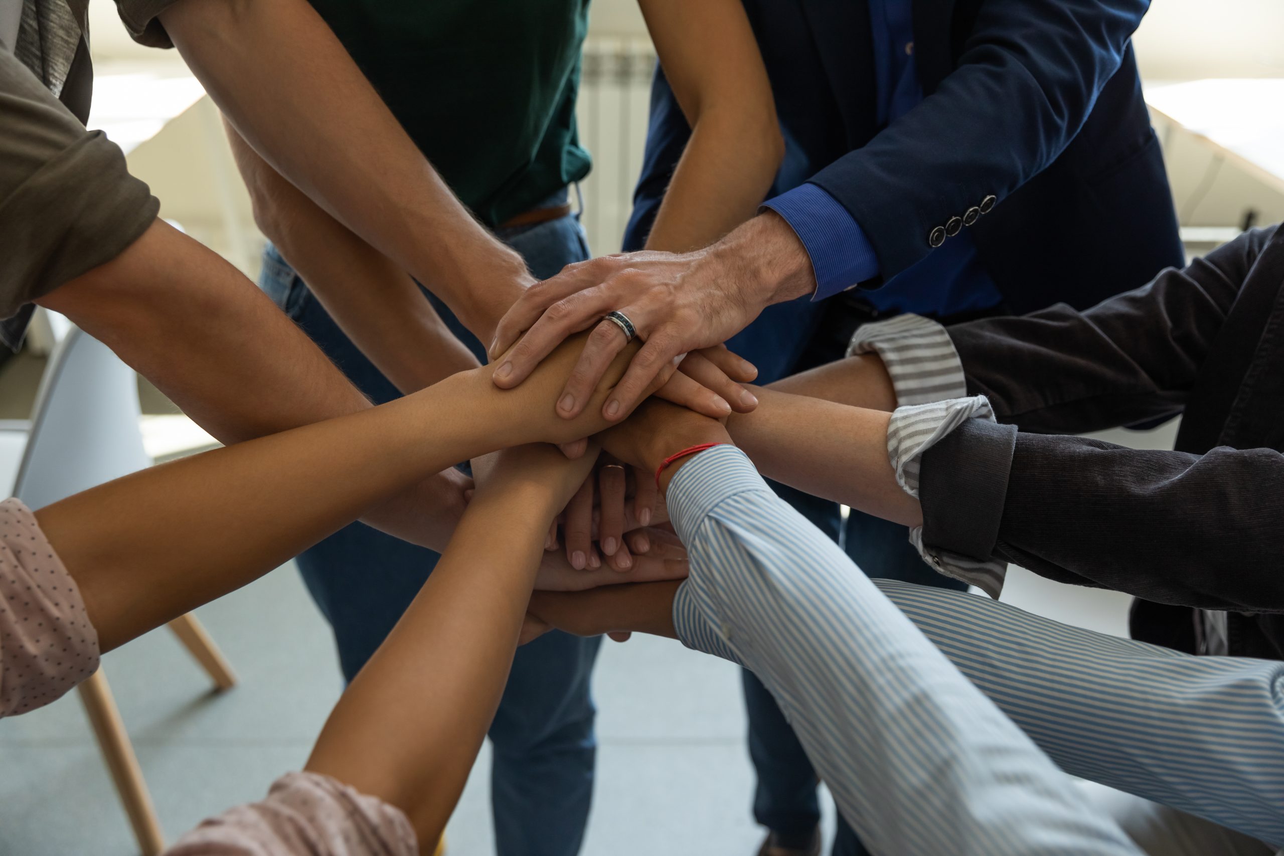 A group of arms from diverse individuals including skin cover, clothing, gender and age overlap hands in the center of a circle. Adobe Stock Image