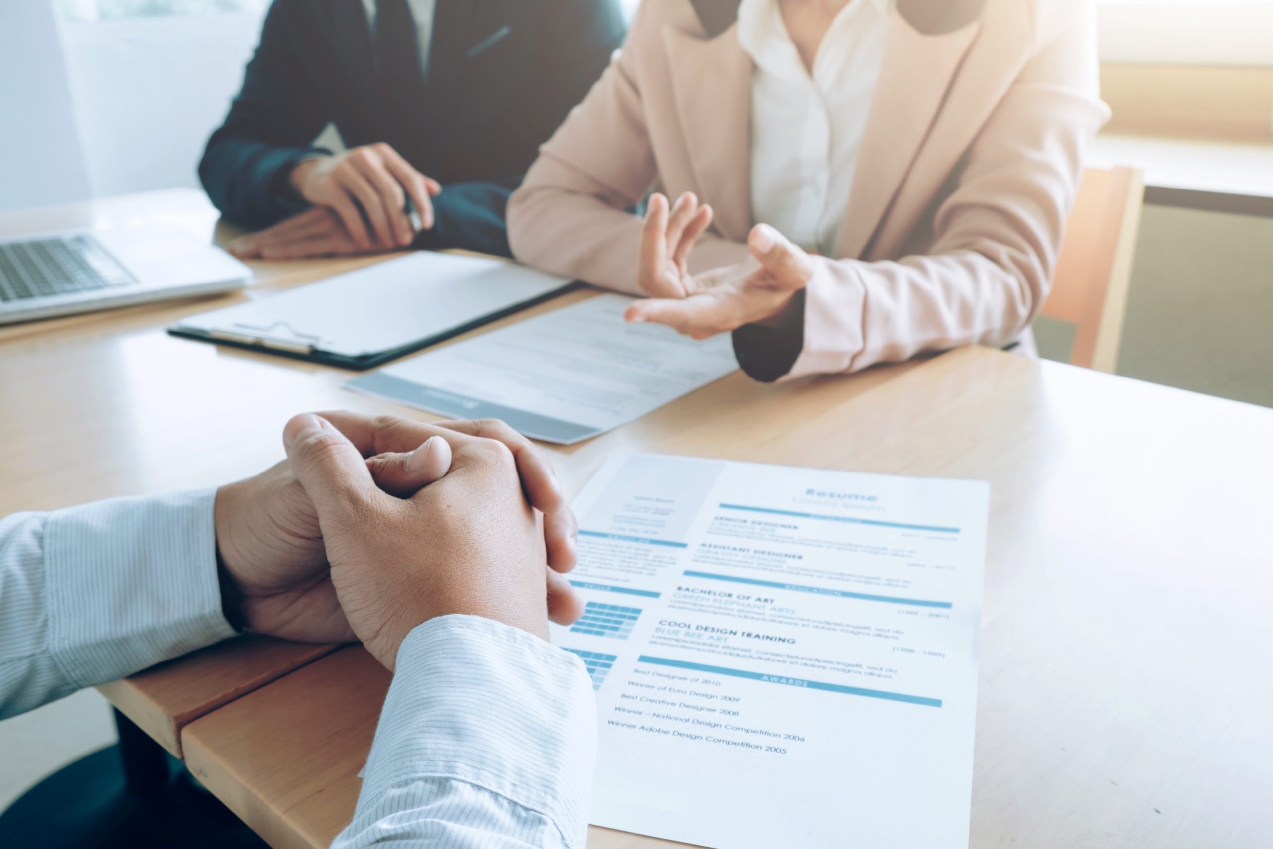 One person sits across a table from two others with a resume and clipboards in front of each person. Adobe Stock Image