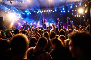 Crowd of people standing to watch a rock band on the stage in front of them. Adobe Stock Image