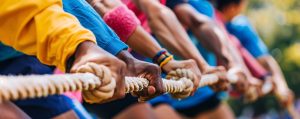 Multiple hands hold a rope for tug of war. Adobe Stock