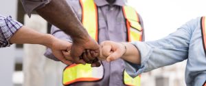 Three workers in safety vests fist bumping, symbolizing teamwork and solidarity. Adobe Stock