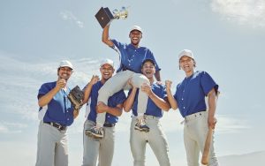 Five baseball players celebrating; one is lifted while holding a trophy, symbolizing victory. Adobe Stock