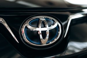 Close-up view of the Toyota logo on a vehicle featuring metallic ellipses with a blue background indicating Toyota’s hybrid products. Adobe Stock