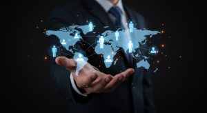 Person in a suit holding a digital world map with connected icons of people, symbolizing global networking and collaboration. Adobe Stock